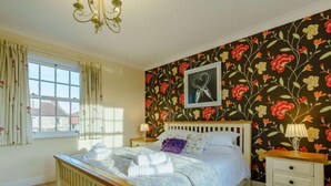 A bedroom with a bed, a nightstand, a lamp, a window with curtains, and a floral wallpaper. - 3 Bed in Richmond (oc-90578) (Catterick)