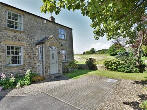 A stone house with a paved driveway and a grassy lawn.