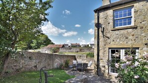 A stone building with a garden patio, a water pump, and a view of houses in the background. - 3 Bed in Richmond (oc-90578) (Catterick)