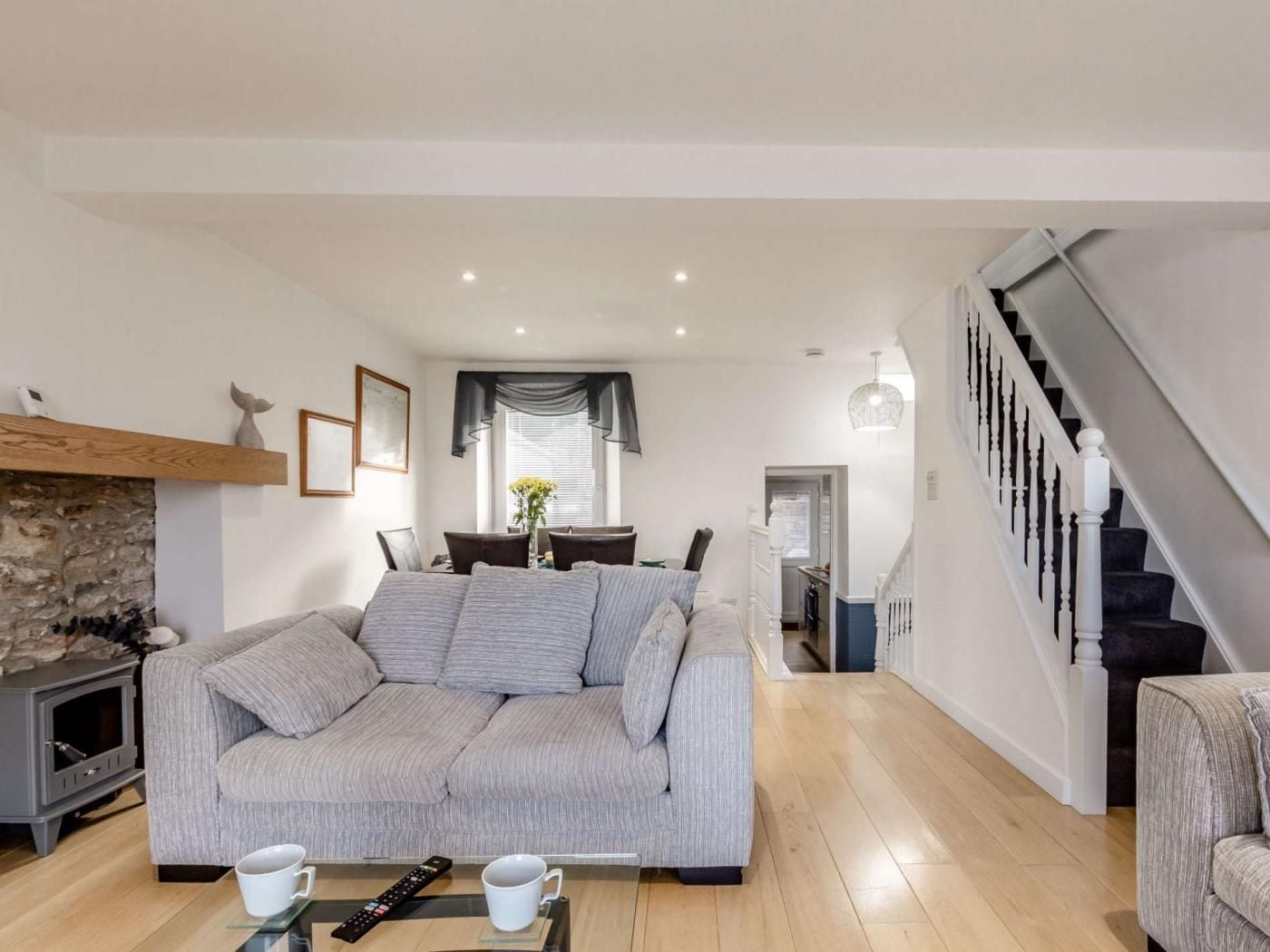 A living room with a grey sofa, a fireplace, a dining area, and a staircase.