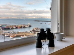 Fernglas und eine weiße Tasse auf einem Fensterbrett mit Blick auf einen Hafen.