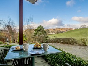 A table with plates and mugs, a chair, and a view of a green landscape with hills. - 1 Bed in Ambleside (oc-90637) (Ambleside)
