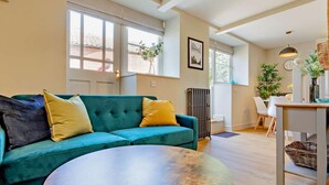 Ein Wohnzimmer mit einem türkisfarbenen Sofa, einem runden Couchtisch und einem Essbereich mit Tisch und Stühlen.