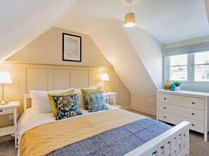 A bedroom with a sloped ceiling, a bed with patterned bedding, bedside lamps, a dresser, and a window with a view. - 2 Bed in Fakenham (oc-90682) (Fakenham)