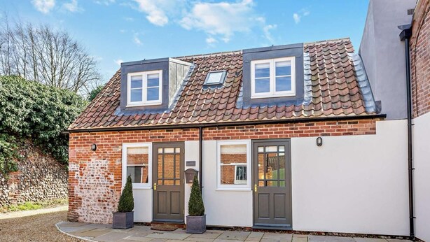 Ein zweistöckiges Haus mit Ziegeldach, Backsteinfassade und einer Veranda mit zwei Blumentöpfen.