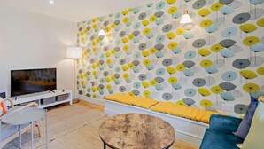 Ein Wohnzimmer mit Wandmuster, einer Couch, einem Couchtisch, einem Fernseher und einer Lampe.