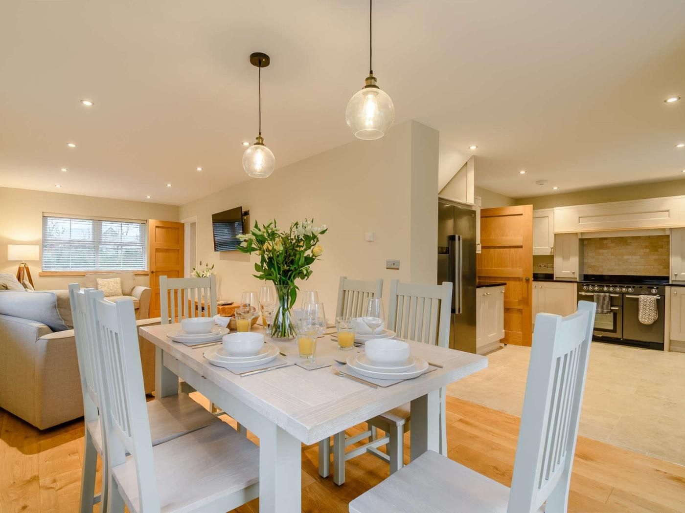 A dining area with a white table set for four, surrounded by white chairs, with a vase of flowers on the table.