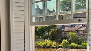 A window with a view of a garden, a stone wall, and a building with a tiled roof. - 3 Bed in Hawes (oc-90749) (Hawes)