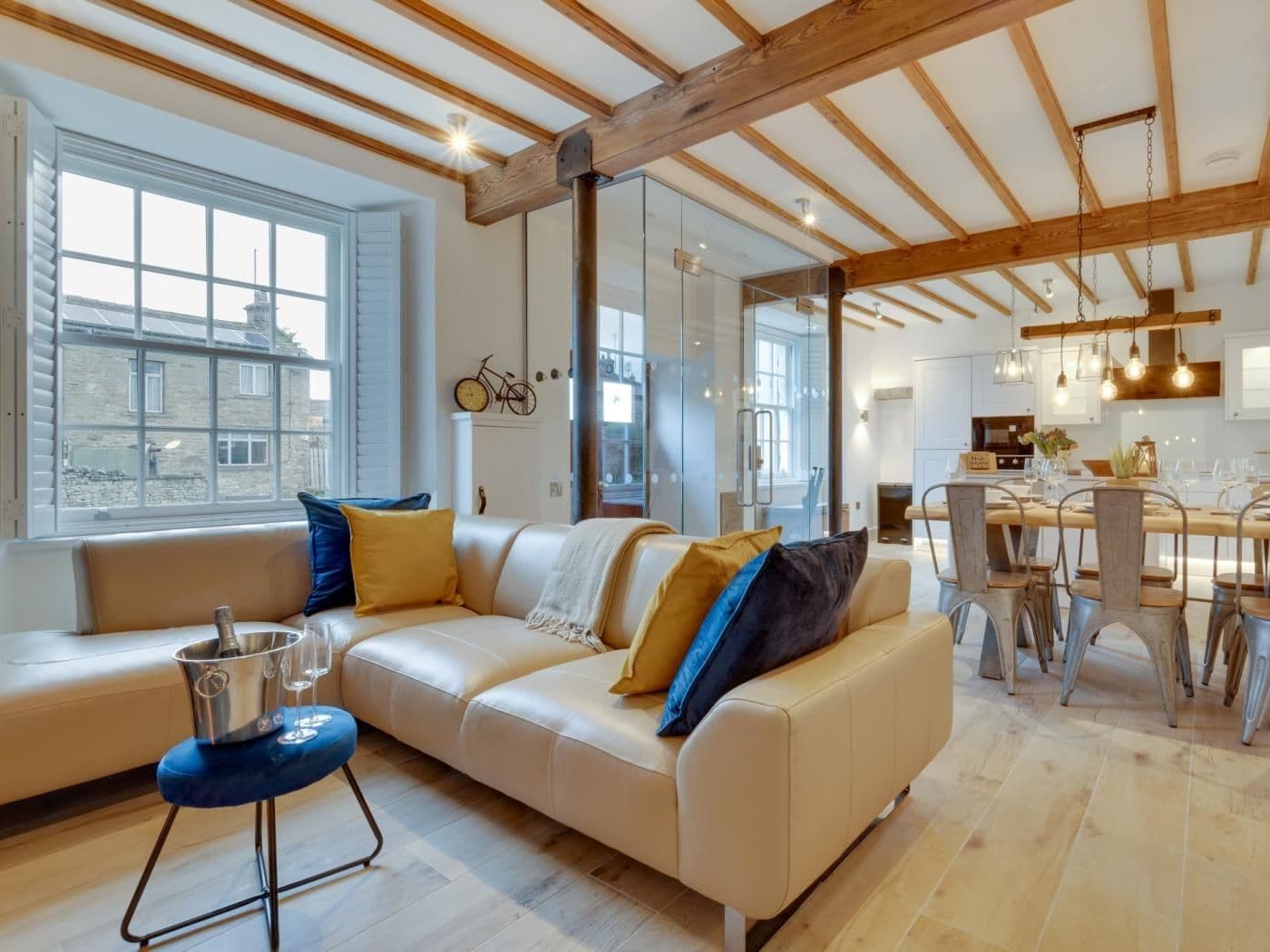 Uma sala de estar moderna com um sofá, área de jantar com mesa e cadeiras, e cozinha ao fundo.