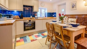 Una cocina moderna con una isla central, un comedor con mesa y sillas de madera, y una alfombra colorida.