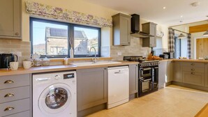 Een moderne keuken met een ingebouwde wasmachine, vaatwasser en oven, grote ramen en uitzicht op het omliggende gebied.
