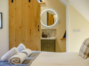 Une chambre à coucher avec un lit, une armoire en bois, une salle de bain avec un miroir et un luminaire rond.