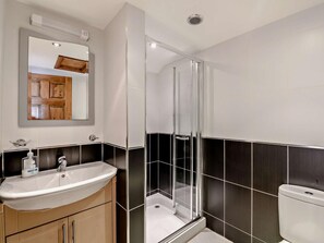 Ein modernes Badezimmer mit einem weißen Waschbecken, einem Spiegel, einer Duschkabine und dunkel gefliesten Wänden.