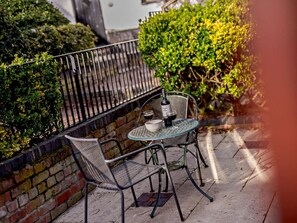 Eine Terrasse mit einem runden Tisch, zwei Stühlen, einer Weinflasche und einer Schüssel.