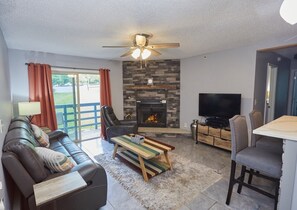 A living room with a sofa, a coffee table, a fireplace, a TV, and a dining area. - Slopeside Condo - sleeps 4- Walk to Timberline Mountain ski lifts and lodge! (Tucker County)