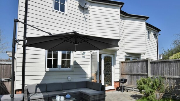 A house with a covered patio, a grey outdoor sofa, and a barbecue grill. - 3 Bed in Whitstable (oc-91063) (Whitstable)