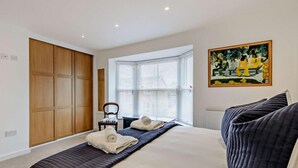 A bedroom with a bed, a window with blinds, a chair, and a painting on the wall. - 3 Bed in Whitstable (oc-91063) (Whitstable)