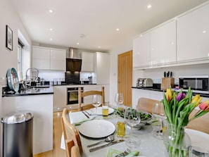 A modern kitchen with white cabinets, a central island, and a dining area set for a meal. - 3 Bed in Whitstable (oc-91063) (Whitstable)