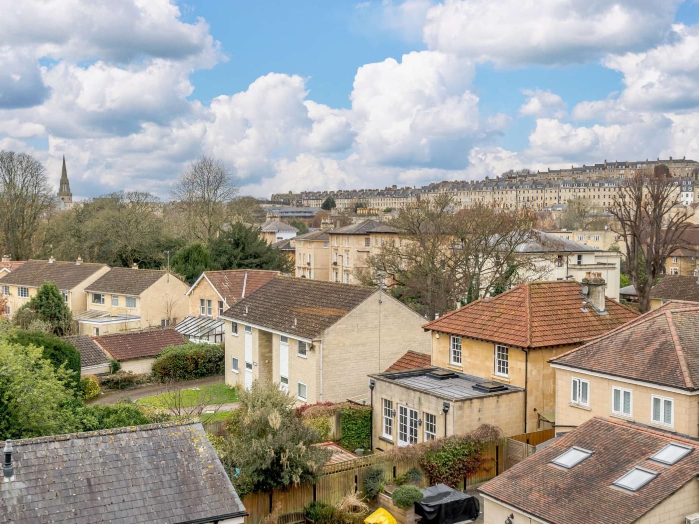 A residential area with houses, a church spire, and a hill in the background.