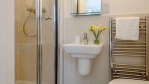 Baño con cabina de ducha de vidrio, lavamanos pedestal, espejo y perchero.