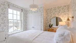 Un dormitorio con una cama grande, un tocador, un espejo y una ventana con papel tapiz floral.