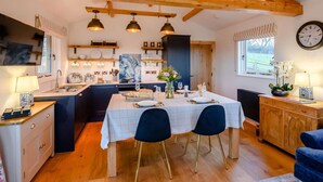 A spacious kitchen with wooden beams, a dining area with a table set for four, and a clock on the wall. - 2 Bed in Leyburn (oc-91102) (Finghall)