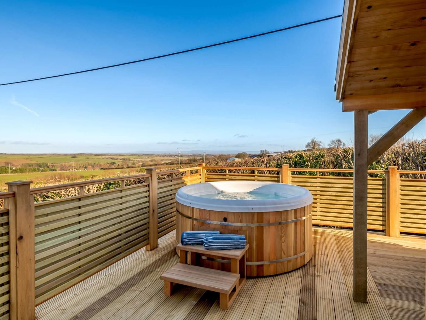 A wooden deck with a hot tub, a bench, and a view of the countryside.