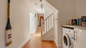 A hallway with a wooden floor, a staircase, a washing machine, and a bookshelf with books. - 2 Bed in Tenby (oc-91092) (Tenby)
