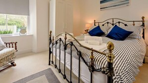 A bedroom with a bed, a chair, a wardrobe, and a painting on the wall. - 2 Bed in Tenby (oc-91092) (Tenby)