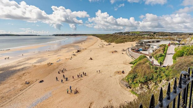 A beach with people, a building, and a clear sky. - 2 Bed in Tenby (oc-91092) (Tenby)
