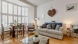 A spacious living room with a glass coffee table, a sofa, a dining area with chairs, and large windows. - 2 Bed in Tenby (oc-91092) (Tenby)