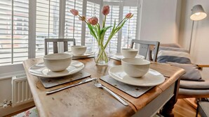 A dining table with white bowls and plates, a vase with flowers, and a chair. - 2 Bed in Tenby (oc-91092) (Tenby)