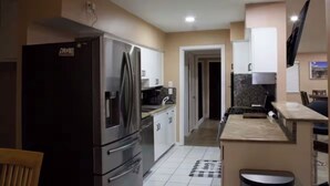 Uma cozinha moderna com eletrodomésticos de aço inoxidável, uma sala de jantar com mesa e cadeiras, e uma TV fixada na parede.