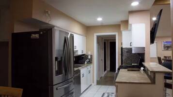 A modern kitchen with stainless steel appliances, a dining area with a table and chairs, and a TV mounted on the wall.