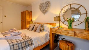 A neatly made bed with a plaid blanket, a bedside table with a lamp, a mirror, and a heart-shaped wall decoration. - 2 Bed in Alnwick (oc-91316) (Alnwick)