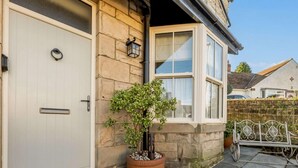 A house with a white door, stone exterior, a window with white frames, and a potted plant on the porch. - 2 Bed in Alnwick (oc-91316) (Alnwick)