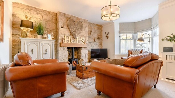 A cozy living room with a stone fireplace, leather sofas, a television, and a chandelier. - 2 Bed in Alnwick (oc-91316) (Alnwick)