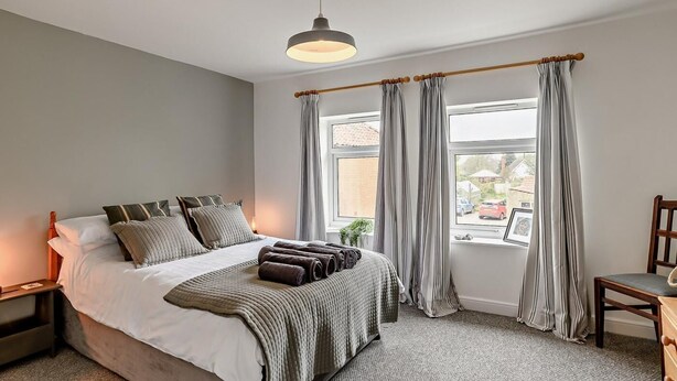 A bedroom with a bed, a bedside table, a chair, a window with curtains, and a hanging light fixture. - 2 Bed in Melton Constable (oc-91371) (Briston)