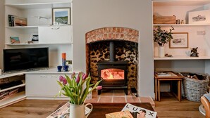 A living room with a fireplace, a TV, shelves with books and decorations, and a table with a vase of flowers. - 2 Bed in Melton Constable (oc-91371) (Briston)