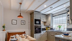 A kitchen with wooden cabinets, a dining table set with dishes, and a hanging light fixture. - 2 Bed in Melton Constable (oc-91371) (Briston)