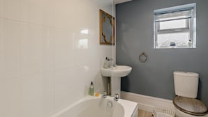 A bathroom with white tiles, a bathtub, a sink, a toilet, and a window with a view. - 2 Bed in Melton Constable (oc-91371) (Briston)
