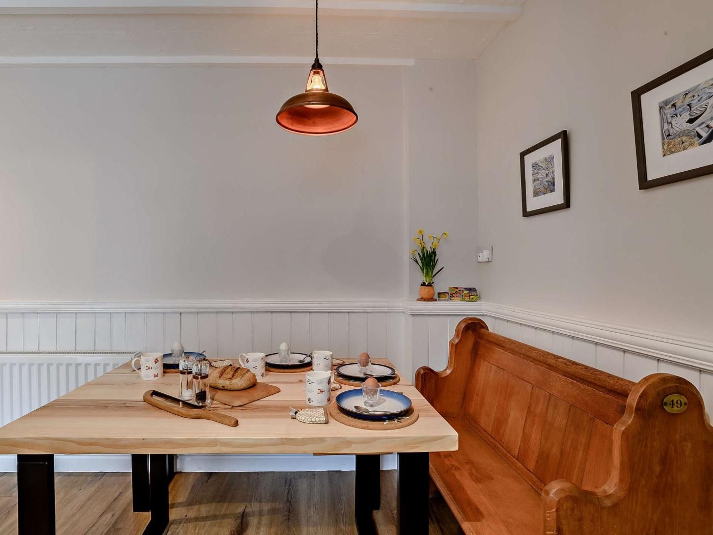 A dining area with a wooden table, benches, and a hanging light fixture.