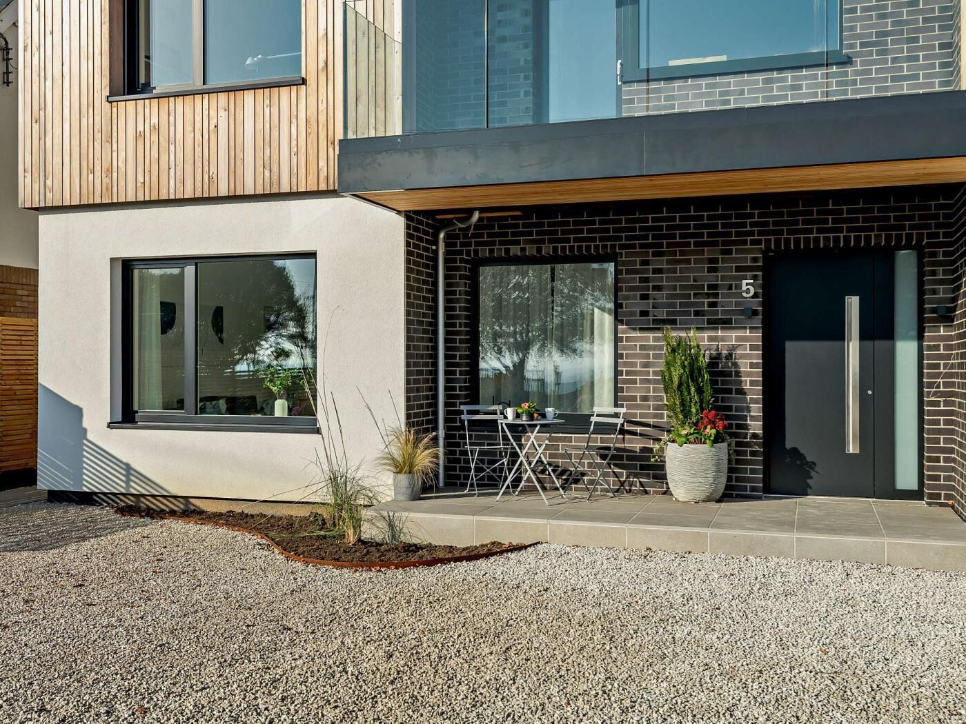 A modern building with a brick facade, large windows, and a gravel driveway.