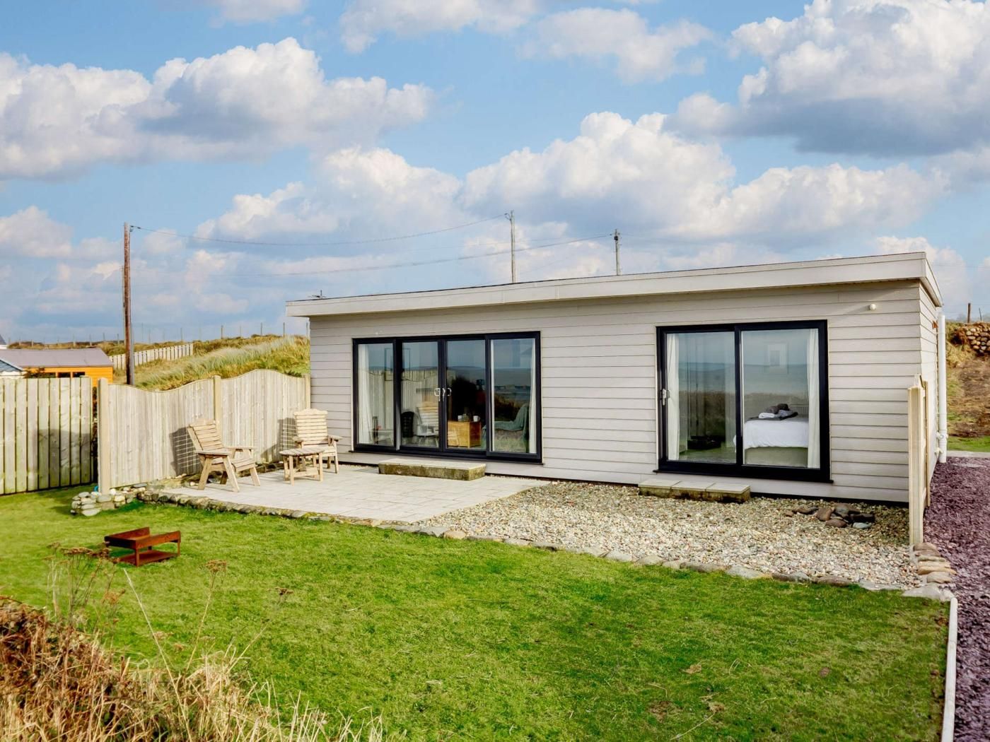 A modern single-story house with a patio area, a wooden fence, and a grassy lawn.