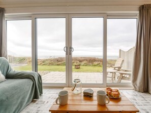 A room with a bed, a table with mugs and pastries, and a view through large glass doors to an outdoor seating area.