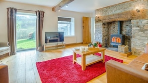 A living room with a stone fireplace, a television, and a red rug. - 5 Bed in Brecon (oc-90660) (Lower Chapel)