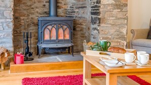 A cozy room with a stone fireplace, a wooden table with breakfast items, and a comfortable seating area. - 5 Bed in Brecon (oc-90660) (Lower Chapel)