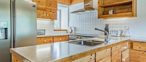 Una cocina moderna con armarios de madera, un refrigerador de acero inoxidable, horno empotrado y una isla grande con pileta.