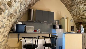 A kitchen with a stone ceiling, grey cabinets, a white refrigerator, a microwave, and two black bar stools. - Old stone sheepfold: charm and authenticity in the heart of nature. Dog, okay. (Saint-Beauzély)