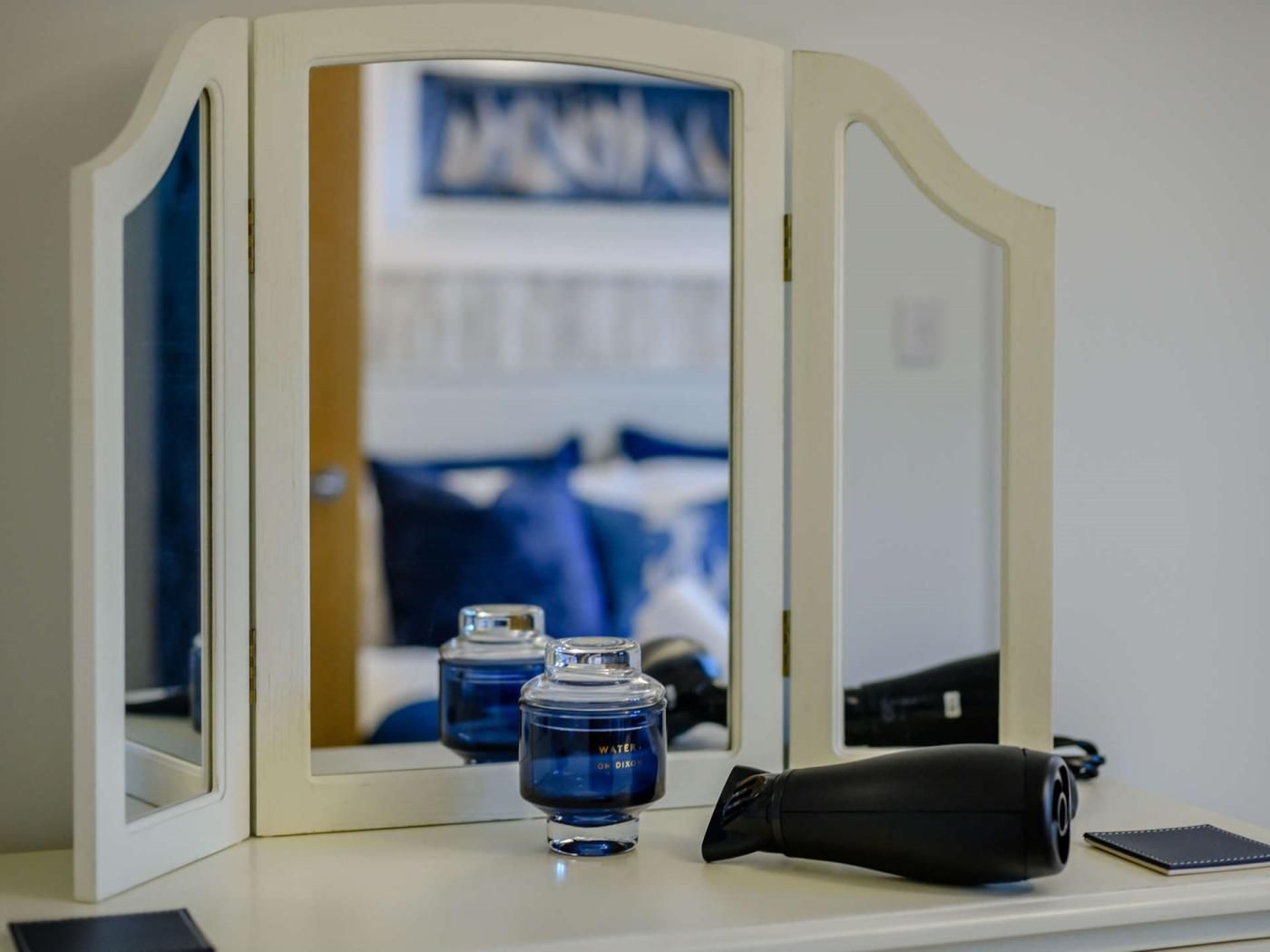A vanity with a mirror, two blue water bottles, and a black object on a white surface.